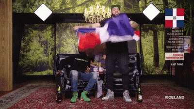 Two Men Are Sitting On A Couch With A Sign That Says Viceland On It GIF