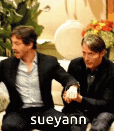 Two Men Are Sitting On A Couch With The Name Sueyann On The Bottom Right GIF