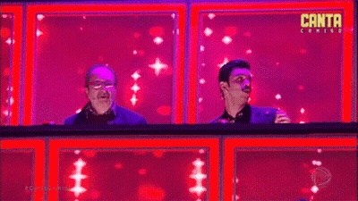 Two Men Are Sitting On A Stage In Front Of A Pink Background . GIF