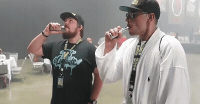 Two Men Are Smoking Electronic Cigarettes And One Has A Shirt That Says E Liquids On It GIF