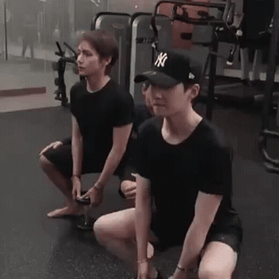 Two Men Are Squatting Down In A Gym While Holding Dumbbells . GIF