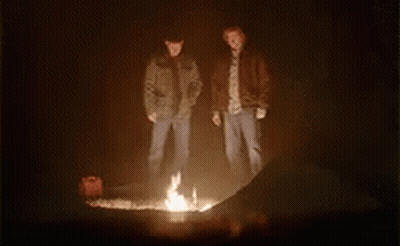 Two Men Are Standing Around A Fire In The Dark . GIF