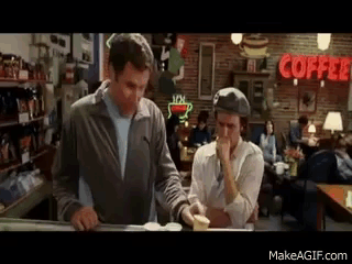 Two Men Are Standing At A Counter In A Coffee Shop With A Coffee Sign In The Background . GIF