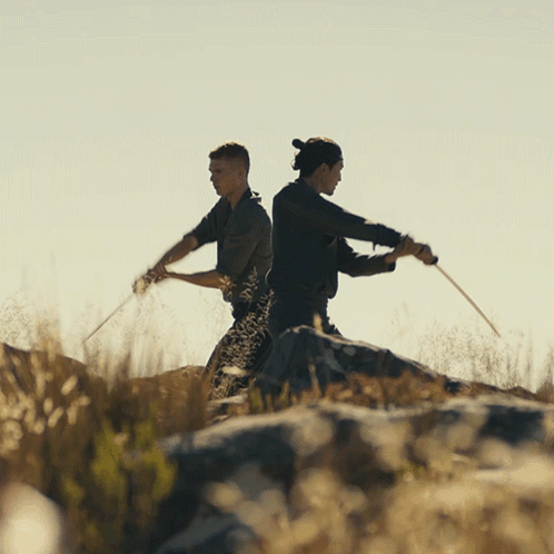 Two Men Are Standing Back To Back Holding Swords GIF