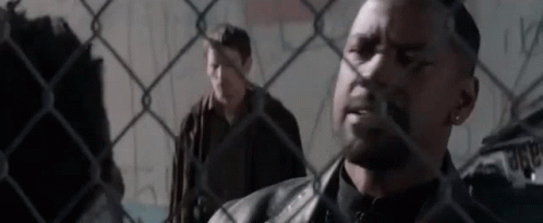 Two Men Are Standing Behind A Chain Link Fence . GIF