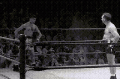 Two Men Are Standing In A Boxing Ring With A Crowd Watching Them . GIF