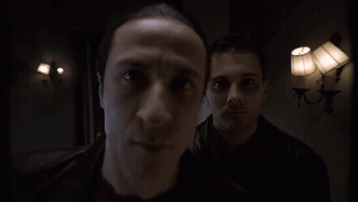 Two Men Are Standing In A Dark Room With Lamps On The Wall GIF
