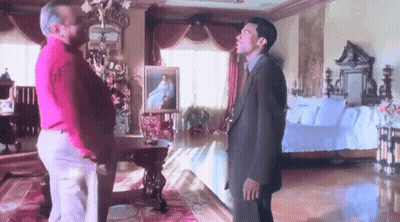 Two Men Are Standing In A Room With A Couch And A Painting On The Wall GIF