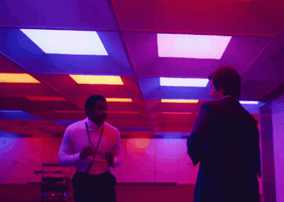 Two Men Are Standing In A Room With Purple And Red Lights On The Ceiling GIF