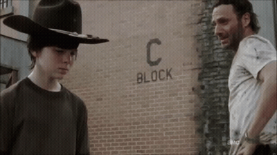 Two Men Are Standing In Front Of A Brick Wall That Says Block C. GIF