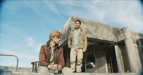 Two Men Are Standing In Front Of A Building With A Blue Sky Behind Them GIF