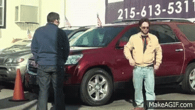 Two Men Are Standing In Front Of A Car Dealership With A Sign That Says 215-613-5331 GIF