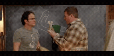 Two Men Are Standing In Front Of A Chalkboard With A Drawing Of A Penis On It GIF