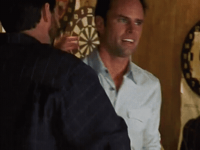 Two Men Are Standing In Front Of A Dart Board And One Is Holding A Dart GIF