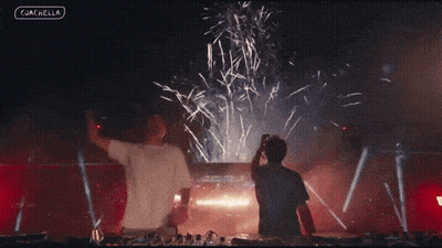 Two Men Are Standing In Front Of A Fireworks Display And The Words Coachella Are On The Bottom Left GIF