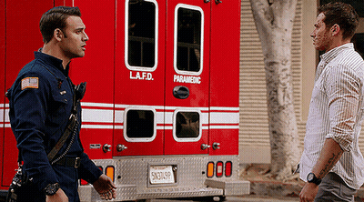 Two Men Are Standing In Front Of A Lafd Paramedic Vehicle GIF
