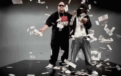 Two Men Are Standing In Front Of A Pile Of Money And One Of Them Is Wearing A Shirt That Says ' Famous ' On It GIF