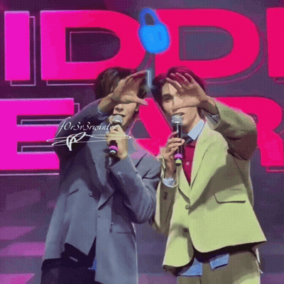 Two Men Are Standing In Front Of A Pink Sign That Says Id Ear GIF