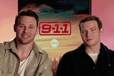 Two Men Are Standing In Front Of A Sign That Says 911 GIF