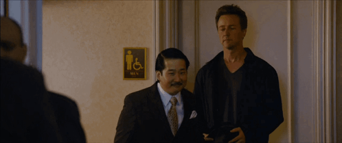 Two Men Standing In Front Of Men's Bathroom Sign GIF