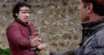 Two Men Are Standing In Front Of A Stone Wall And One Is Wearing A Crown GIF