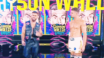 Two Men Are Standing In Front Of A Wall That Says Grayson Waller GIF