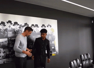 Two Men Are Standing In Front Of A Wall With A Picture Of A Group Of Men GIF