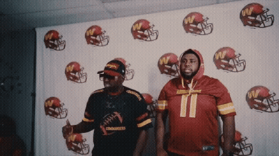 Two Men Are Standing In Front Of A Wall With Football Helmets And One Has The Number 11 On His Jersey GIF