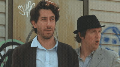 Two Men Are Standing In Front Of A Wall With Graffiti On It That Says Swag GIF