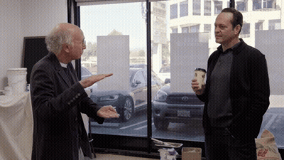 Two Men Are Standing In Front Of A Window With A Sign That Says ' A Few Dollars More ' On It GIF