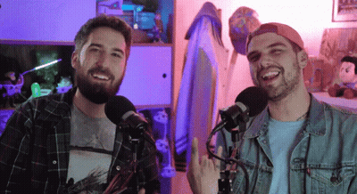 Two Men Are Standing In Front Of Microphones One Is Wearing A Plaid Shirt And The Other Is Wearing A Denim Jacket GIF