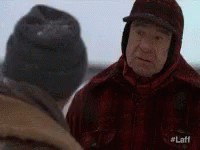 Two Men Are Standing In The Snow And Talking To Each Other . One Of The Men Is Wearing A Hat . GIF