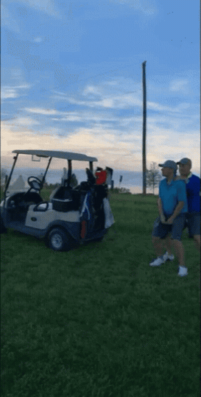 Two Men Are Standing Next To A Golf Cart On A Grassy Field GIF