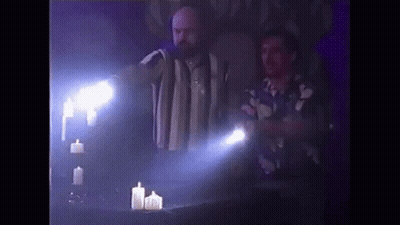 Two Men Are Standing Next To A Table With Candles And A Flashlight . GIF