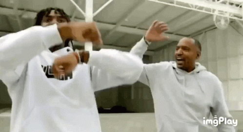 Two Men Are Standing Next To Each Other And Elbow Bumping Each Other In A Room . GIF