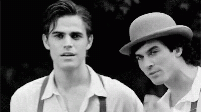 Two Men Are Standing Next To Each Other In A Black And White Photo . One Of The Men Is Wearing A Bowler Hat . GIF