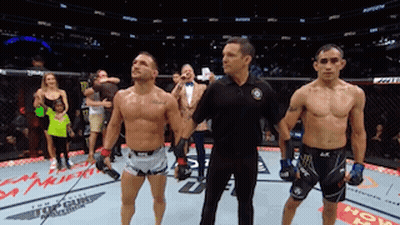 Two Men Are Standing Next To Each Other In A Boxing Ring With A Referee GIF