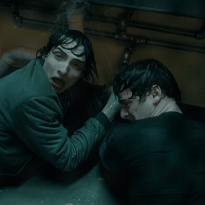 Two Men Are Standing Next To Each Other In A Dark Room And One Is Holding The Other 'S Hand GIF