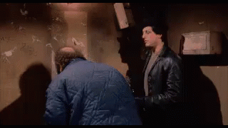 Two Men Are Standing Next To Each Other In A Dark Room And One Of Them Is Holding A Bottle Of Beer . GIF