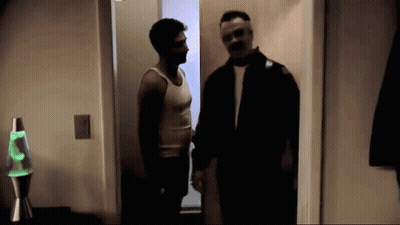 Two Men Are Standing Next To Each Other In A Dark Room With A Green Lava Lamp In The Background . GIF