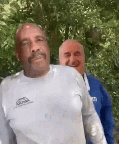 Two Men Are Standing Next To Each Other In A Forest . GIF