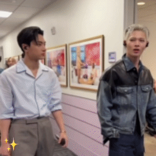 Two Men Are Standing Next To Each Other In A Hallway With Paintings On The Wall . GIF