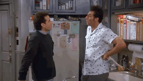 Two Men Are Standing Next To Each Other In A Kitchen Talking . GIF