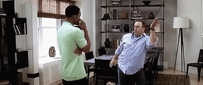 Two Men Are Standing Next To Each Other In A Living Room . One Of The Men Is Talking On A Cell Phone . GIF