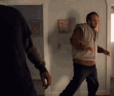 Two Men Are Standing Next To Each Other In A Living Room . One Of The Men Is Wearing A Hoodie . GIF