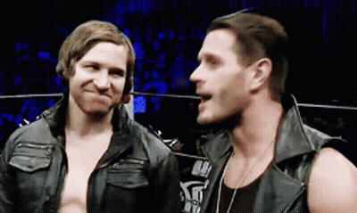 Two Men Are Standing Next To Each Other In A Ring And One Of Them Is Wearing A Leather Vest GIF