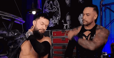 Two Men Are Standing Next To Each Other In A Room . One Of The Men Is Wearing A Leather Jacket . GIF
