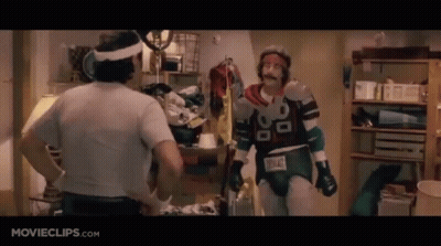 Two Men Are Standing Next To Each Other In A Room . One Of The Men Is Wearing A Superhero Costume . GIF