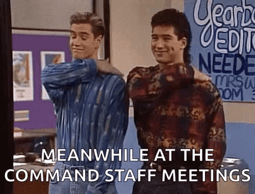Two Men Are Standing Next To Each Other In A Room With A Sign That Says Meanwhile At The Command Staff Meetings . GIF