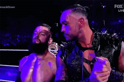 Two Men Are Standing Next To Each Other In A Wrestling Ring . One Of The Men Is Wearing A Leather Vest . GIF